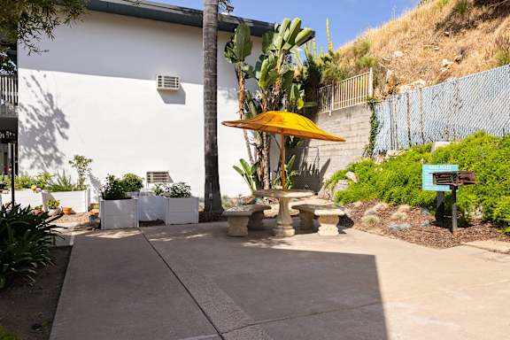 A patio area with a yellow umbrella and a white building in the background.