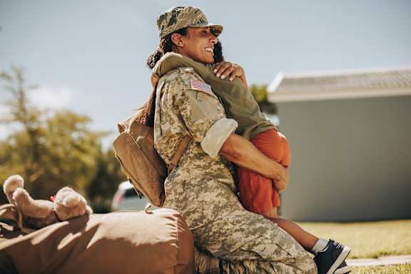 A woman in military uniform is hugging a child.