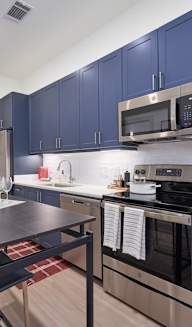 a kitchen with blue cabinets and stainless steel appliances and a black dining table with two blue chairs at Tapestry West in Virginia, 23230