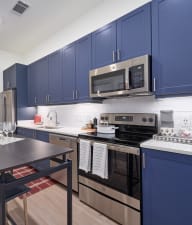 a kitchen with blue cabinets and stainless steel appliances and a black dining table with two blue chairs