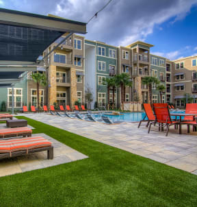 a patio with lounge chairs and a pool in front of an apartment building