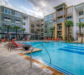 an outdoor pool with lounge chairs and a firepit in front of an apartment building