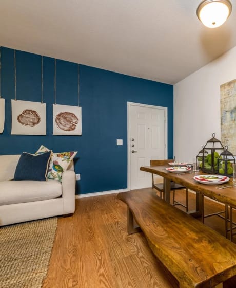 a dining room with a wooden table and bench and a couch in the background at Villa Espada Apartments, San Antonio, Texas