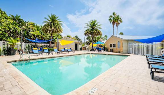 A large outdoor swimming pool surrounded by palm trees and lounge chairs at Coral Club Apartments in Bradenton