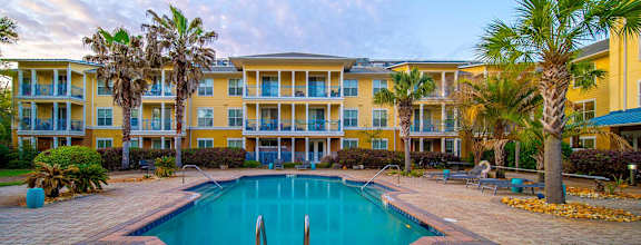 A swimming pool in front of a yellow building with palm trees.