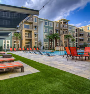 a patio with lounge chairs and a pool in front of an apartment building
