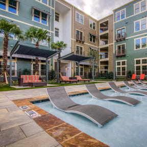 an outdoor pool with chaise lounge chairs and an apartment building in the background
