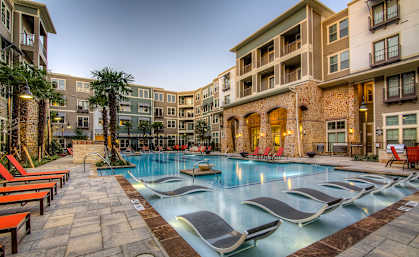a swimming pool with chaise lounge chairs and palm trees in front of an apartment building