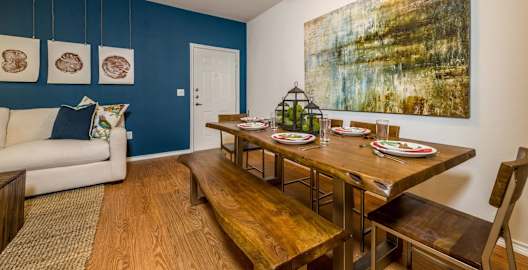 a dining room with a wooden table and bench and a couch in the background at Villa Espada Apartments, San Antonio, Texas