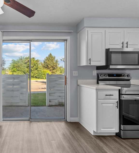 A kitchen with a white oven and microwave, a ceiling fan, and a sliding glass door leading to a backyard.