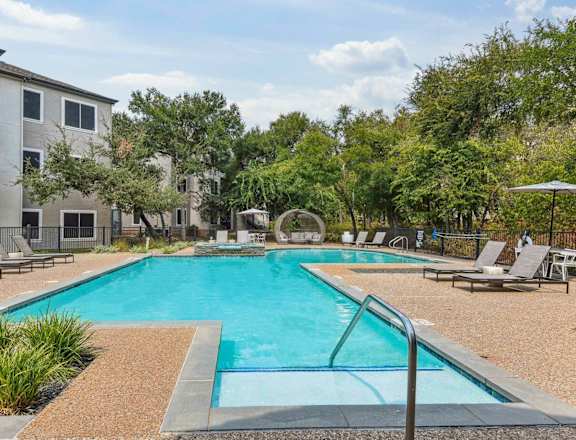 A swimming pool surrounded by lounge chairs and trees.