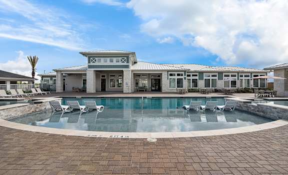 A large swimming pool in front of a building with a blue sky and clouds in the background.