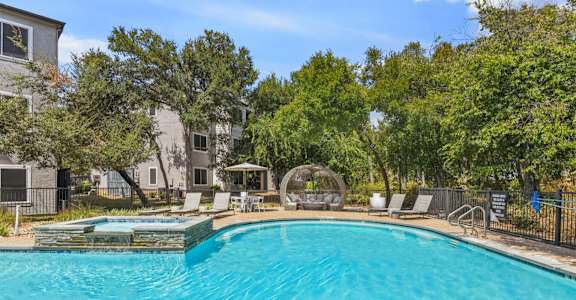 A swimming pool surrounded by trees and chairs.