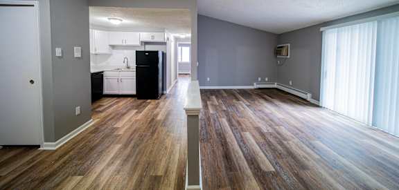 an empty living room with wood floors and a kitchen