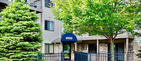 The image shows the entrance to apartment number 9900 in a building surrounded by greenery.
