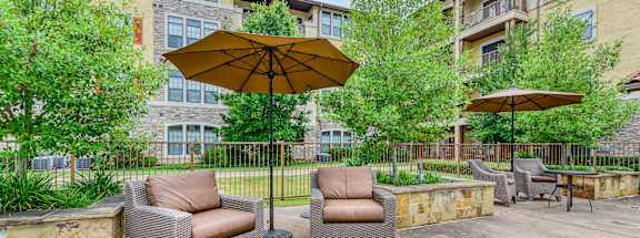 A patio with two chairs and an umbrella in front of a building.