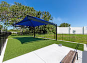 Thumbnail 4 of 7 - A backyard with a blue umbrella and a white fence.