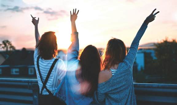 Three people are standing on a bridge with their arms raised in the air.