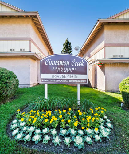 A sign for Cinnamon Creek Apartment is in the foreground of a grassy area.