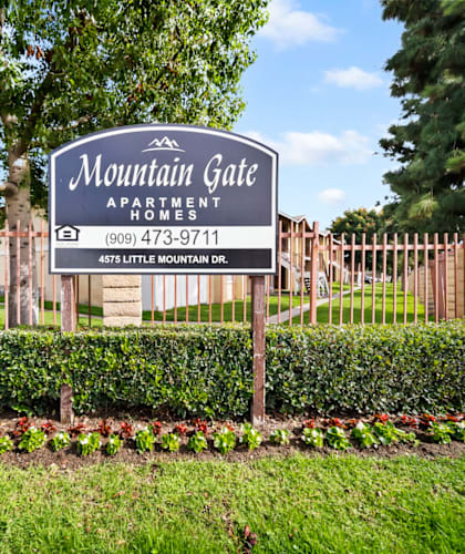 A sign for Mountain Gate Apartment Homes is displayed in front of a fence.