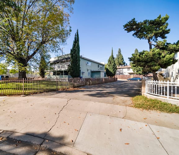 A tree-lined street with a white house and a white fence.