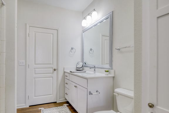 a bathroom with white cabinets and a white toilet next to a white bathtub with a shower