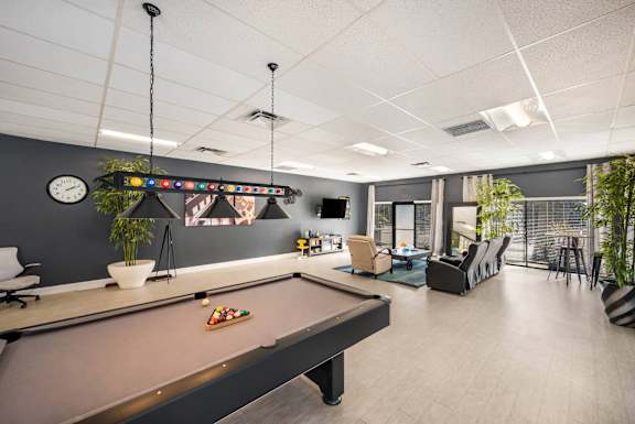 A pool table is in the middle of a room with a clock on the wall.