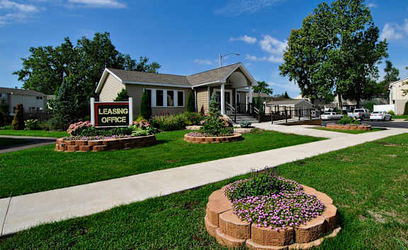 A leasing office is surrounded by greenery and a brick flower bed.