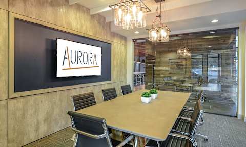A conference room with a long table and chairs, a sign that reads "Aurora" on the wall, and a plant on the table.
