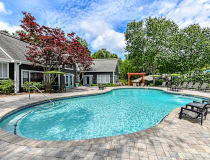 A swimming pool surrounded by a brick patio and lounge chairs.