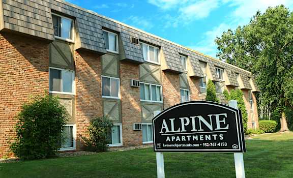A sign for Alpine Apartments stands in front of a brick building.