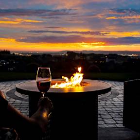 A person is sitting by a fire with a glass of wine.