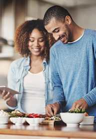 A couple is preparing a meal together in a well-lit kitchen.