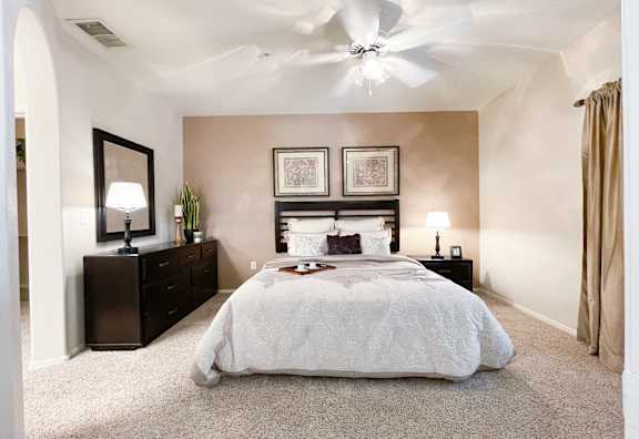 A bedroom with a large bed, a dresser, and a ceiling fan.