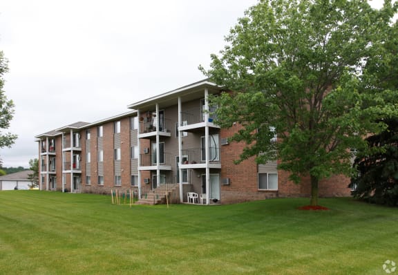 a large grassy area with a tree in front of an apartment building