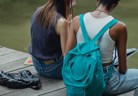 two girls sitting on a dock with a backpack