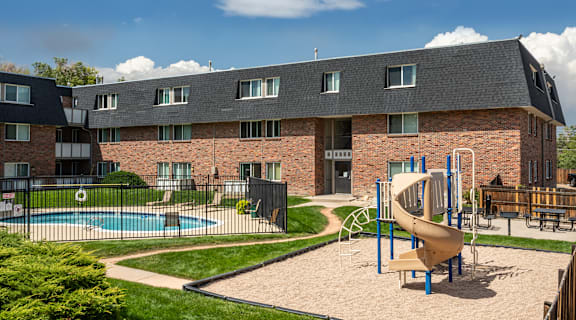 A playground with a slide and swimming pool in front of a brick building.
