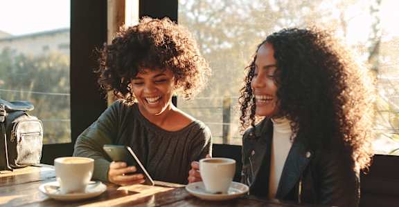 two women sitting at a cafe table looking at a cell phone