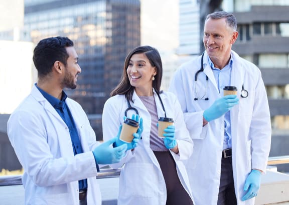a group of doctors in white coats and blue gloves holding coffee cups and talking to each other