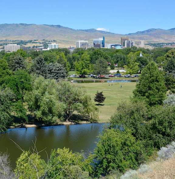 A lake surrounded by trees with a city in the background.