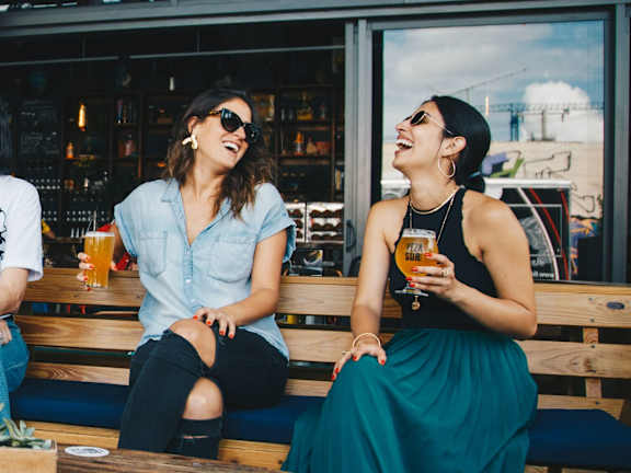 two women laughing and enjoying drinks together while sitting at a table at a bar  at The Tennessee Brewery Apartments, Memphis