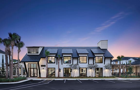 A modern house with a black roof and white walls is surrounded by a parking lot.