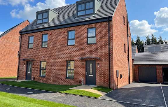A red brick house with a black roof and a grey garage door.