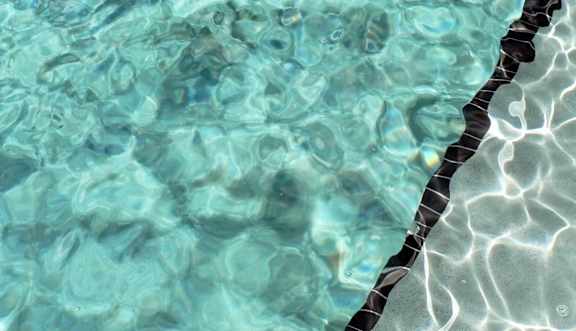 A pool with clear water and a black and white tile edge.
