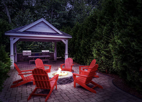 A gazebo with red chairs and a fire pit in the middle of a patio.