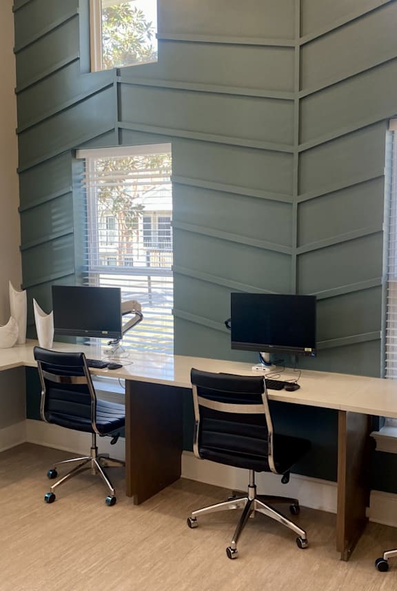 A room with a desk and chairs in front of a window.