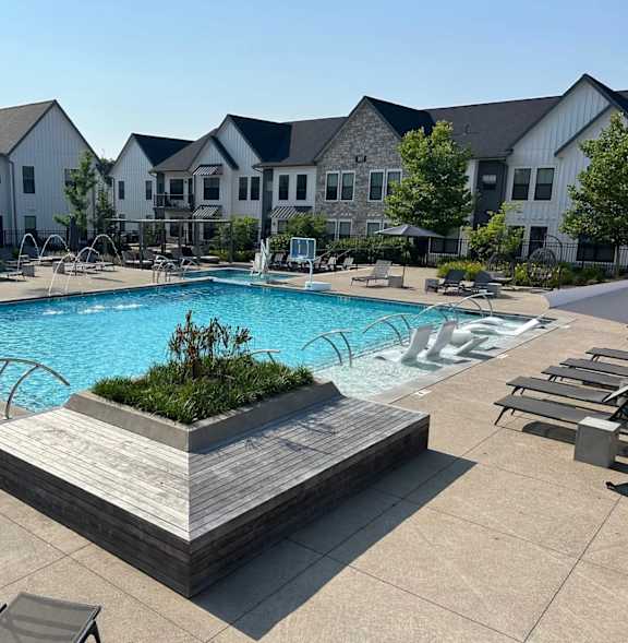 A large swimming pool surrounded by lounge chairs and a wooden deck with a planter in the middle.