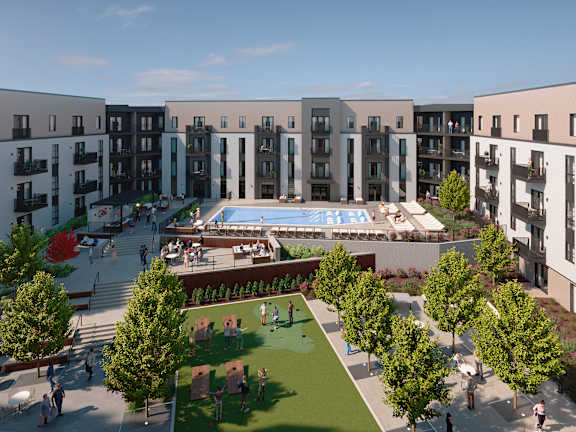 A large outdoor swimming pool surrounded by apartment buildings and a grassy area with people walking and sitting.
