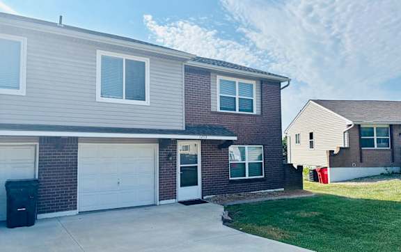 A house with a grey garage door and a red trash bin.