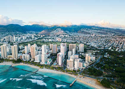 A cityscape with a beach in the foreground and mountains in the background.